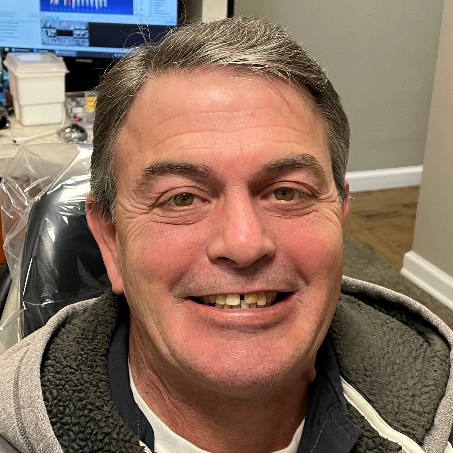 Man smiling at camera in dental office setting wearing dark jacket.