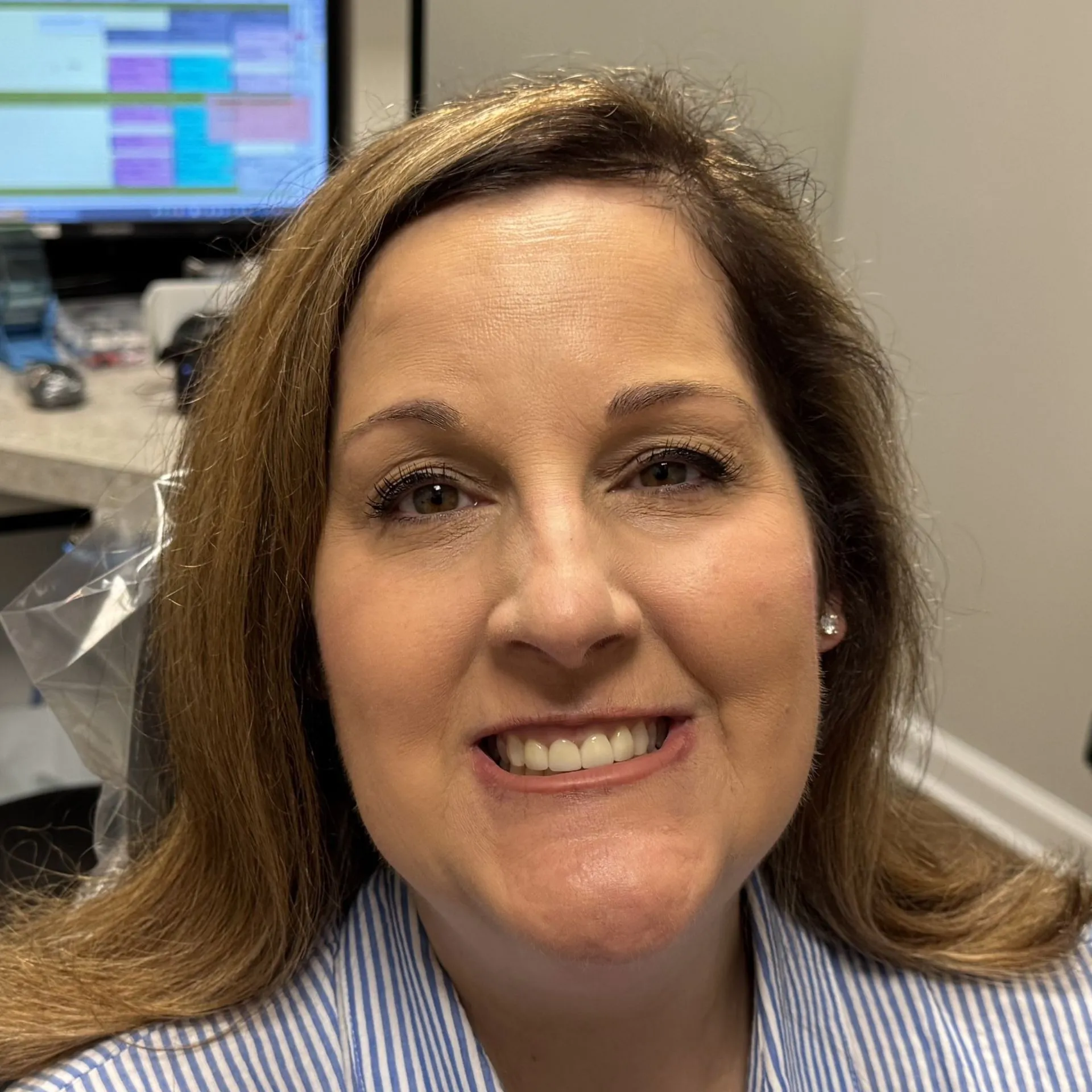 Smiling woman in striped shirt at Pellegrino Dentistry office with computer visible in background.