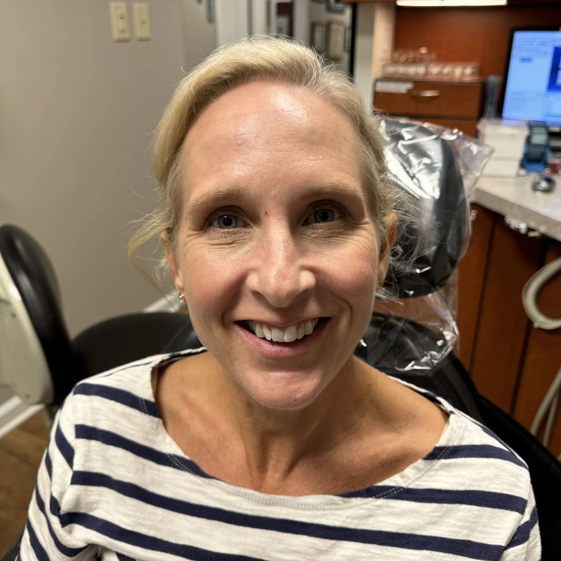 Woman smiling at camera in dental office wearing striped shirt