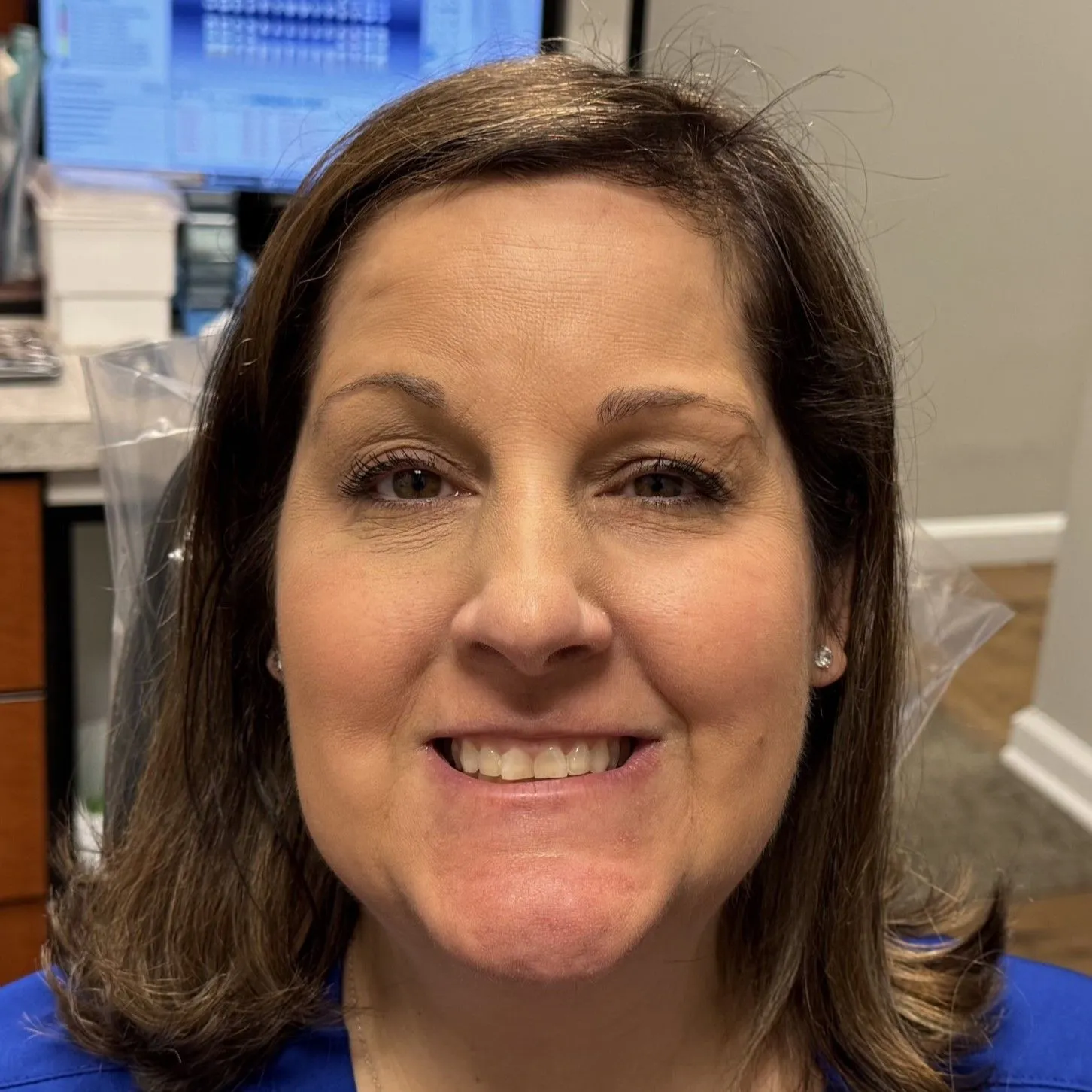 Smiling woman in dental office setting with blue background and equipment visible