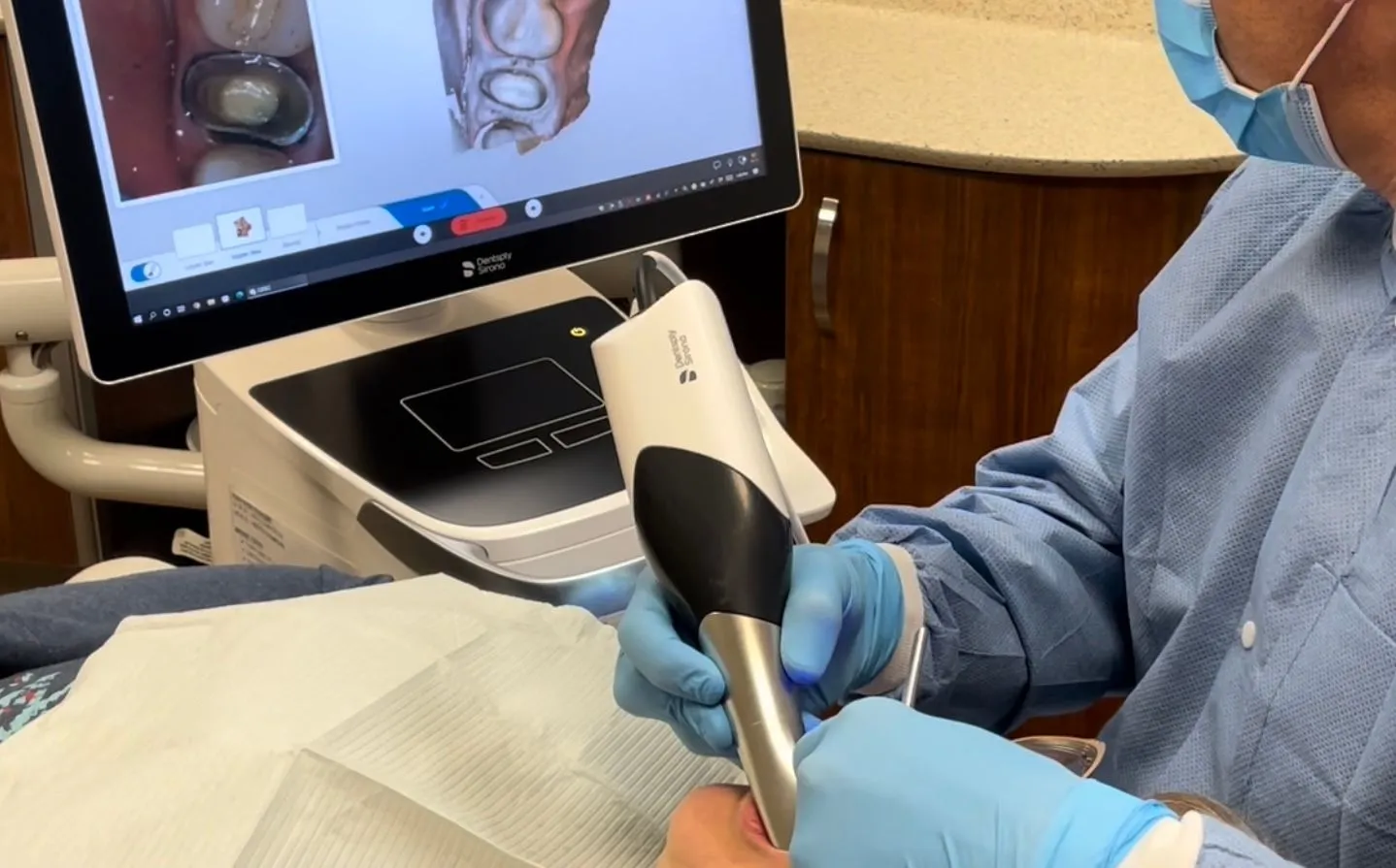 Dentist performing ultrasonic cleaning procedure on patient with digital display showing dental imaging.