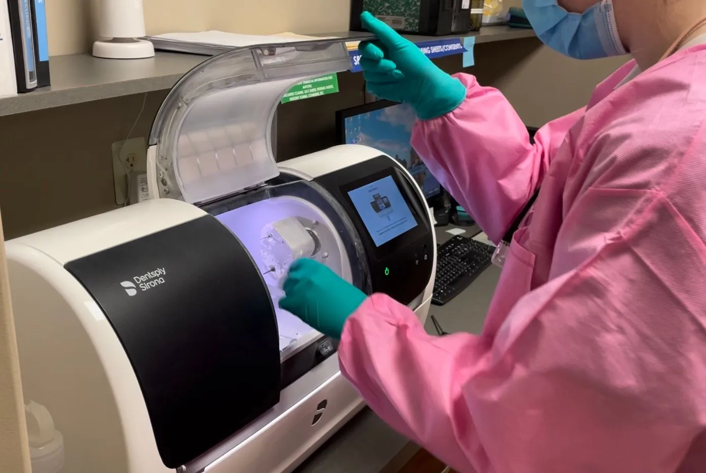 Dental professional in pink scrubs operating laboratory equipment with gloved hands in clinical setting.