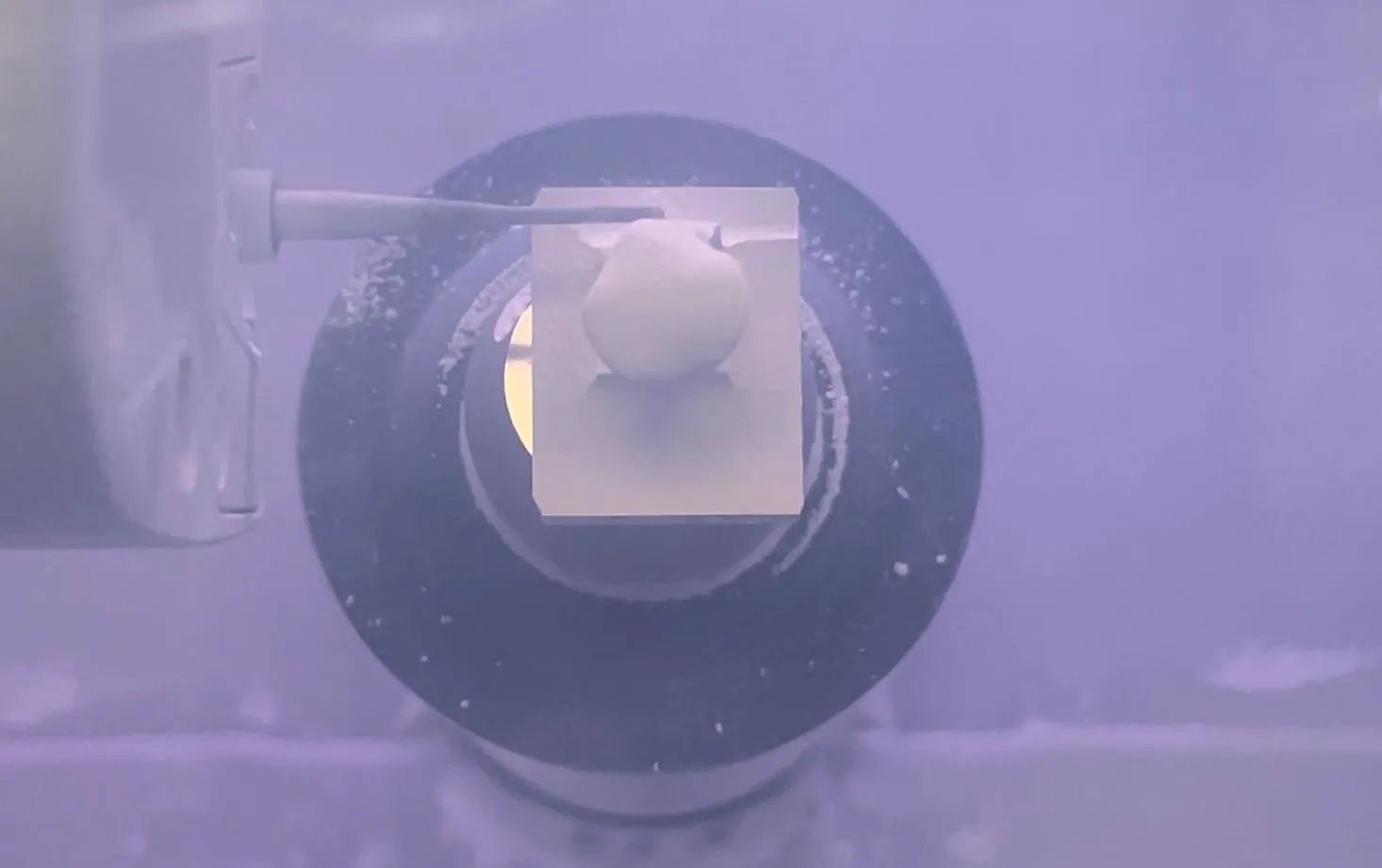 Dental microscope lens viewed through purple-tinted optical equipment in clinical setting.