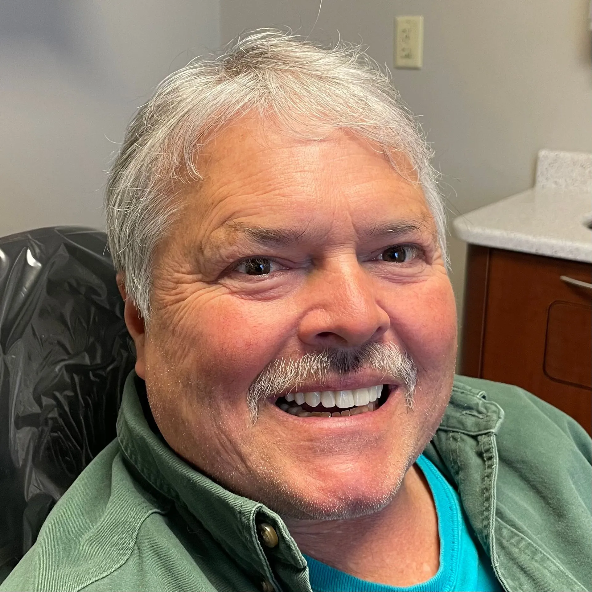 Smiling man in green jacket at dental office, professional headshot portrait.