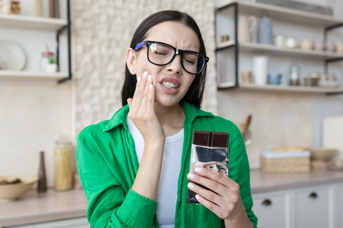 Woman in green jacket holding mobile phone in modern kitchen, smiling at camera.
