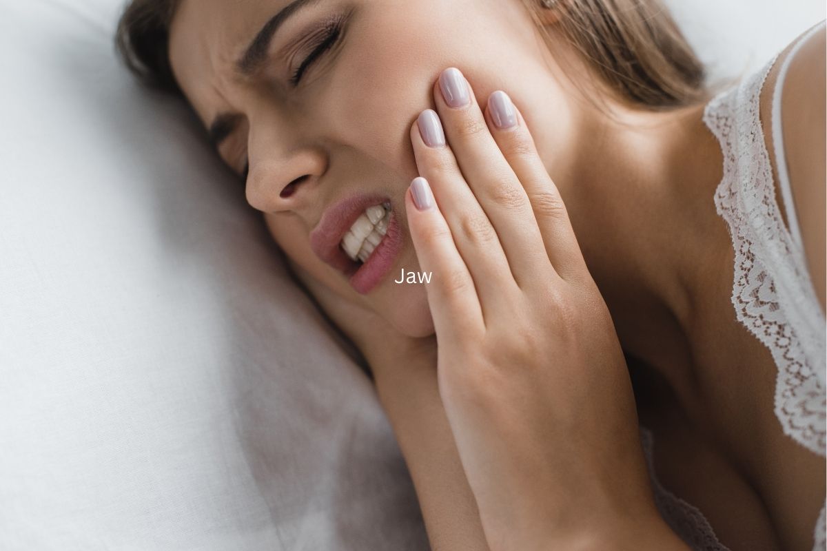 Woman experiencing tooth pain, touching her cheek against white pillow background.