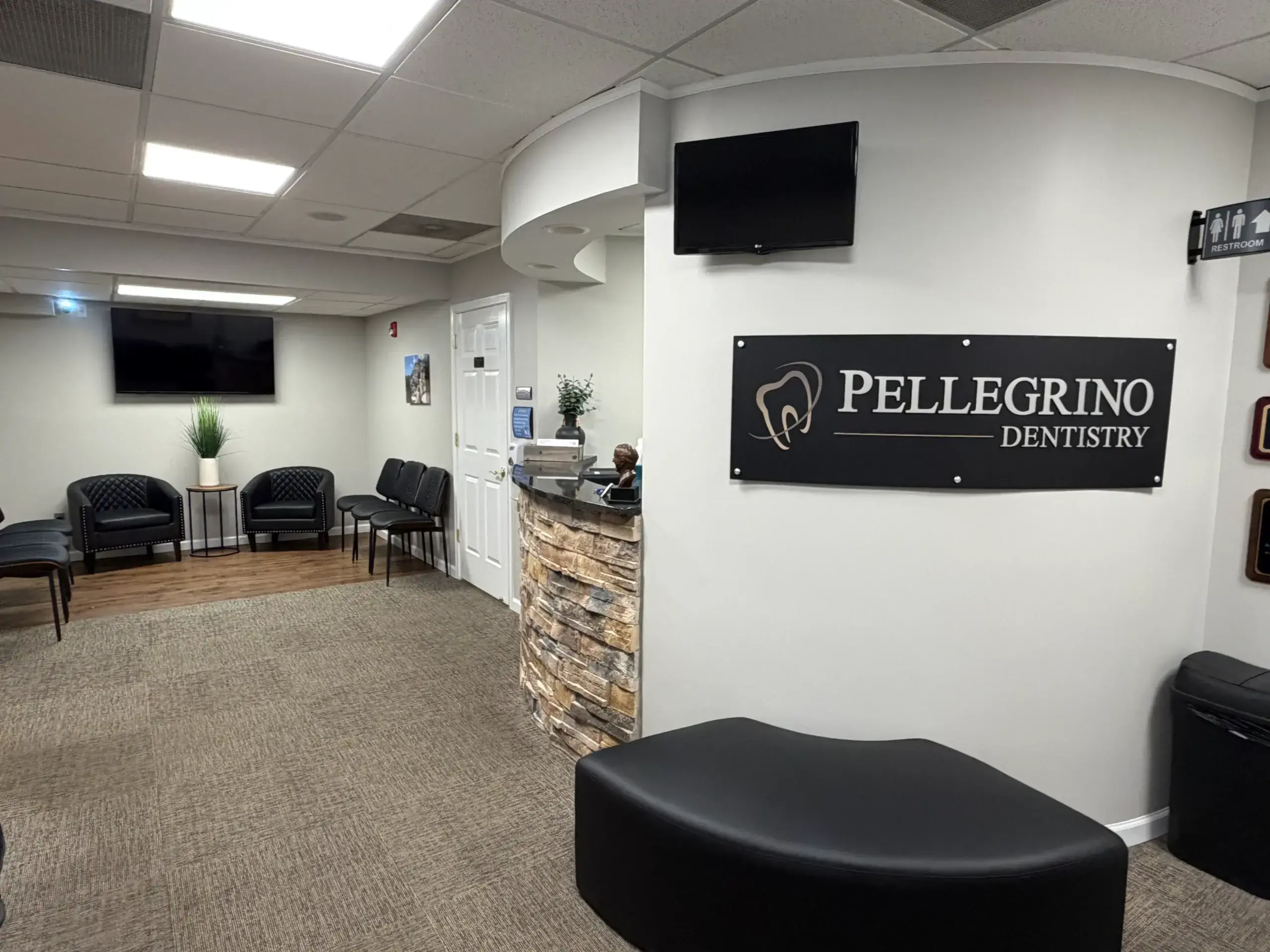 Pellegrino Dentistry waiting room with black leather seating, reception desk, and TV displays.